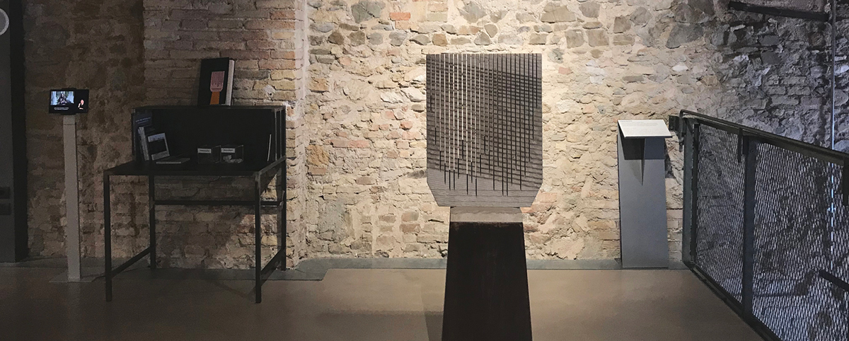 Opera Pietra sonora, accanto didasclia in nero e braille e tavolo con libri e video lis