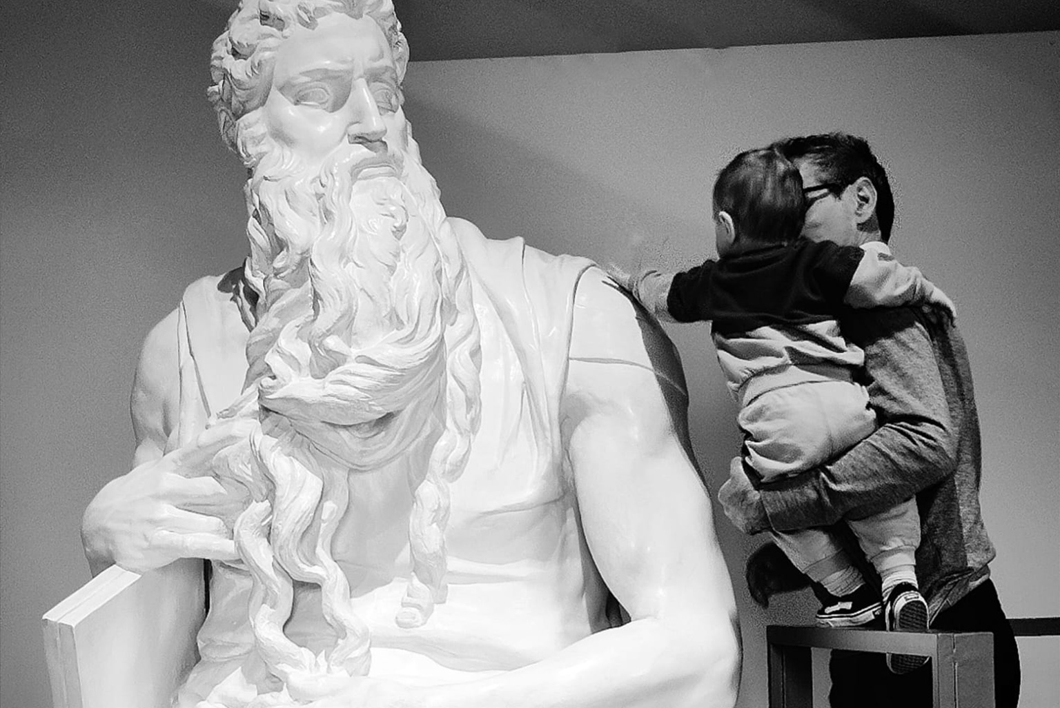 Un adulto tiene in braccio un bambino per fargli toccare la copia del Mosè di Michelangelo