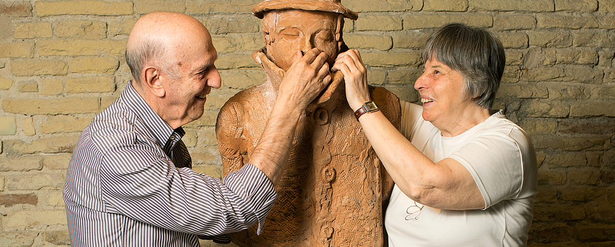 Aldo Grassini e Daniela Bottegoni, entrambi sorridenti, toccano con le mani la scultura L'uomo che imita i cavalli, di Tagliaferri.